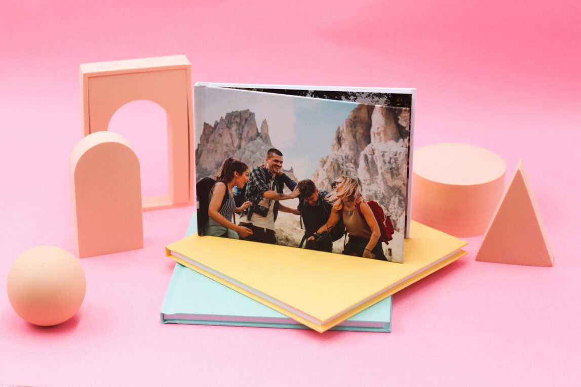 A display showing a printed photobook of people on holiday, stacked on top of yellow and green photobooks.
